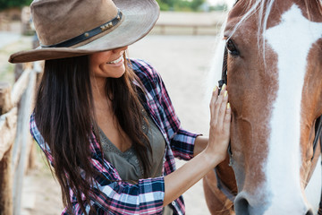 Smiling tender young woman cowgirl in hat with her horse