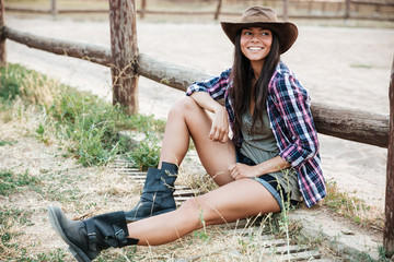 Smiling happy cowgirl sitting and resting at the ranch fence