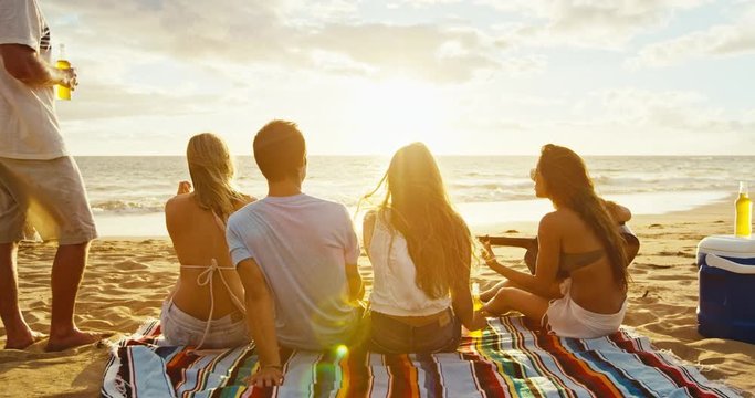 Group of friends having fun relaxing on the beach at sunset