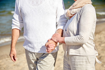 close up of senior couple walking on summer beach
