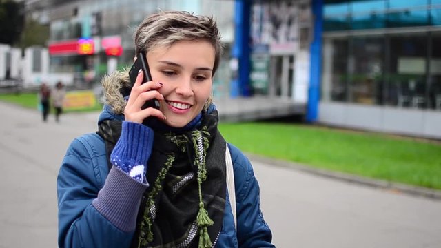 Woman talking on the phone. She walking on the street, smile and move out from the frame.