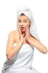 Portrait of surprised girl in spa with clean and fresh skin, happy looking at the camera and touching her face, with a towel on her head , isolated on white background