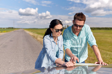 happy man and woman with road map on car hood