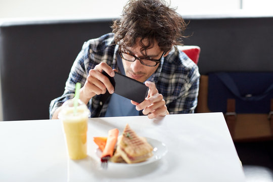 man with smartphone photographing food at cafe