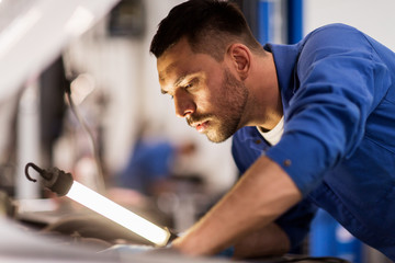 mechanic man with lamp repairing car at workshop