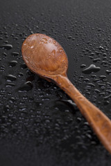 One wooden spoon with water drops on the black 
