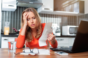 stressed young woman is doing banking and administrative work holding bills at home