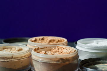 Variety of beauty containers with mineral make-up powder for matt skin on purple background