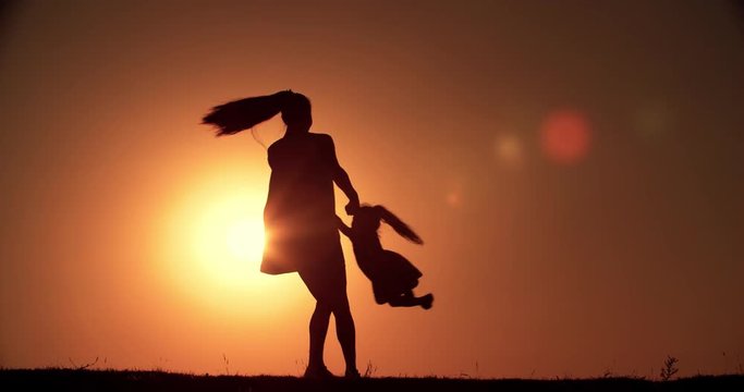 silhouette of mother and little daughter having fun playing at sunset, slow motion