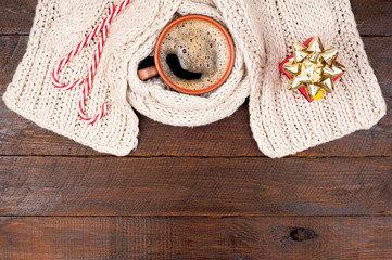 Christmas background. Coffee cup, knitting scarf, present gift box and candy canes on wooden background. Holidays card. Top view