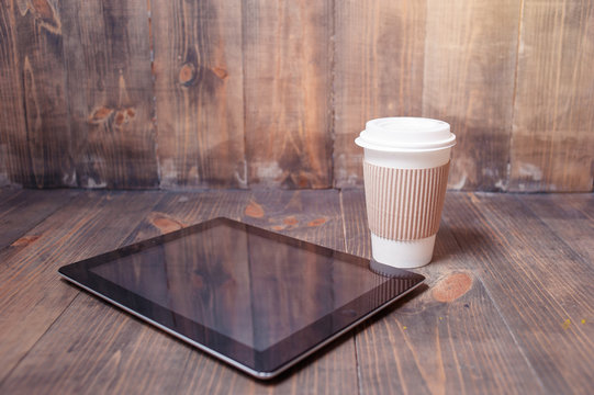 Every Day Essentials. Paper Cup Of Coffee And Tablet Computer On The Wooden Background.