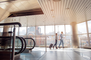 Traveling concept. Happy loving couple in casual wear walking with a luggage by airport terminal.