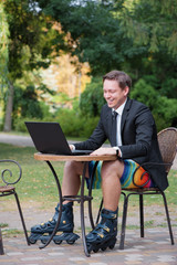 Work and relax. Businessman dressed in suit, shorts and rollers working with laptop at the outdoors...