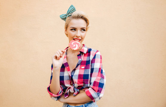 Happy cute pin up girl standing and eating colorful lollipop