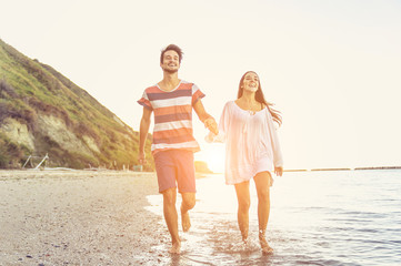 Loving couple running by the sea at sunset