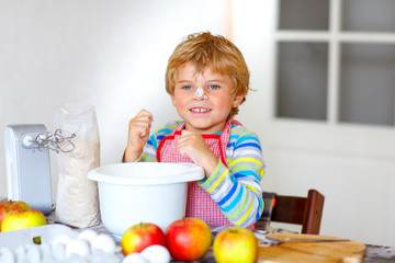 Funny blond kid boy baking apple cake indoors