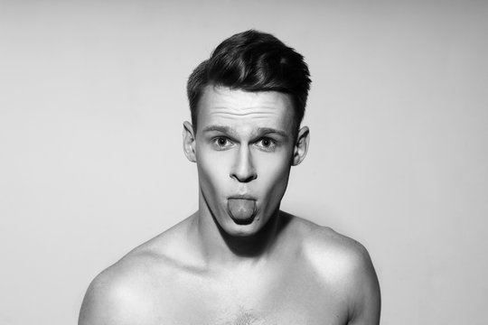 Studio fashion style closeup face portrait of young emotional man looking in camera and showing tongue