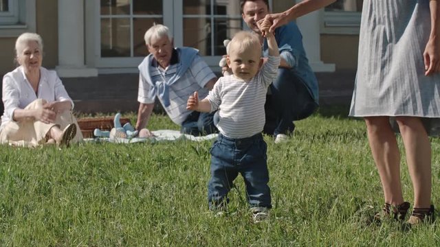 Lockdown of mother holding hand of blond toddler boy and helping him walk, then letting go