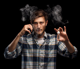 Man is vaping and holding e-liquid. Black background.