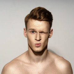 Obraz premium Studio fashion style closeup face portrait of young emotional man giving a kiss and winking