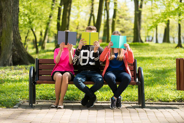 Czytanie książek w parku przez wesołą młodzież szkolną. Wygłupy przy czytaniu. - obrazy, fototapety, plakaty