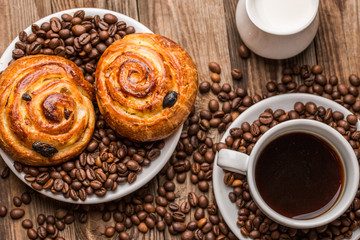 Coffee cup with milk jug and cinnabons on wooden background.
