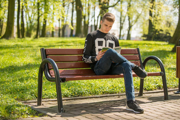 Młody chłopak czyta książkę w parku w słoneczny dzień