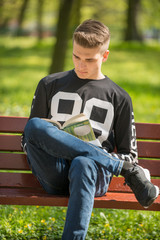 Nastoletni chłopiec czyta książkę na ławce w parku w letni dzień
