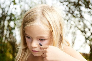 Close up portrait of adorable little child blond girl playing with mommy's make up outside 