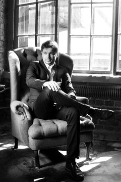 Handsome man in black formal suit with bow-tie sitting in armchair. Black and white fashion style portrait