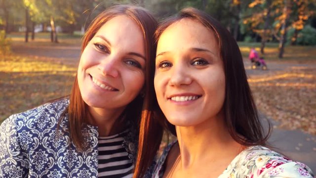 Two nice-looking cheerful girls making selfie photo in autumn park. 3840x2160
