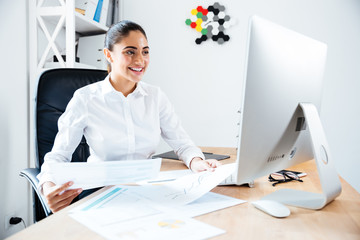 Smiling happy businesswoman holding reports and looking at computer