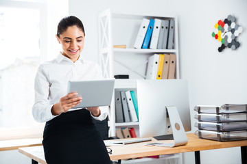 Businesswoman leaning on the office desk and using pc tablet