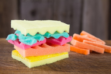 Burger made from sponges different colors on wooden bacground. Concept of unhealthy food and non-natural products