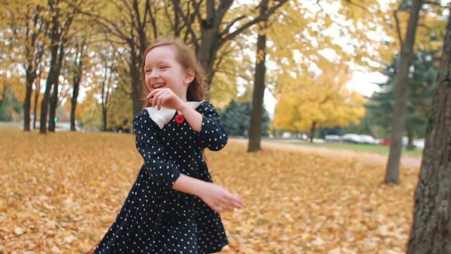 portrait cute little girl with curly hair, in dress with polka dots runing through the autumn alley in the park slow mo