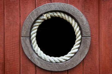 Close-up of a rusty boat porthole rounded with rope against a wood background.