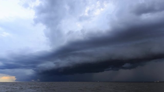 4K Time Lapse : Rain clouds spread across the sky before sunset at sea, estuary, with Cargo ships sail past.