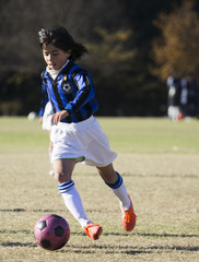 Young girl playing soccer dribbling with ball