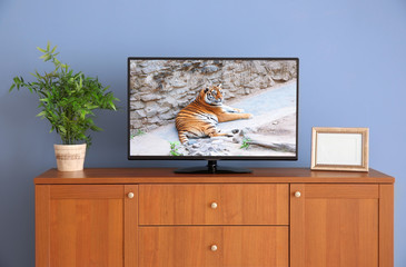 wide screen TV on wooden commode near grey wall
