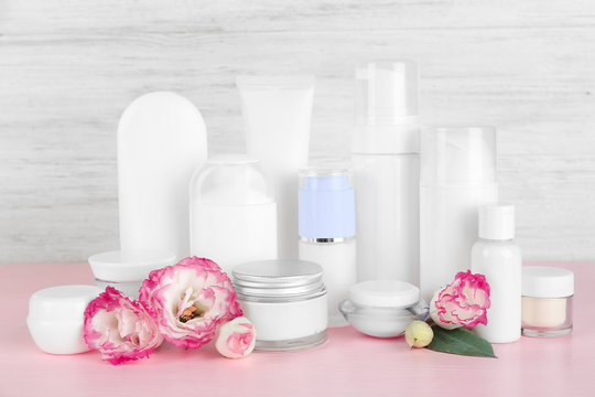 Different cosmetic bottles and flowers on grey wall background