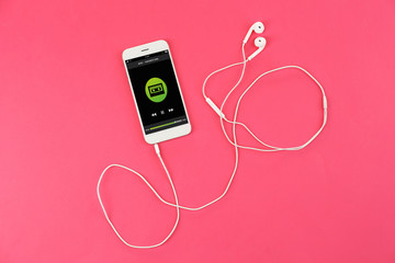 Smartphone with earphones on color background