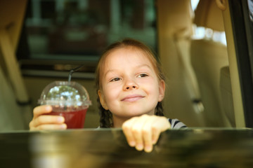Portrait of little girl with glass of juice looking from car window