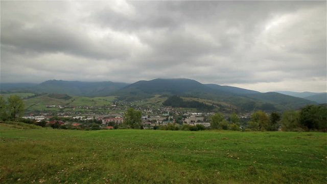 Carpathian mountain landscape with green glade, village in the distance and a mountain with a cloudy sky in background (1080p 25 fps; tripod; canon 7d Mark II, Sigma 10-20)