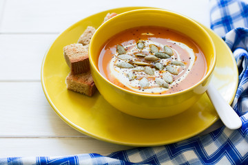 Roasted pumpkin soup with cream and pumpkin seeds on white wooden background