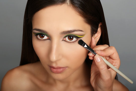 Makeup artist applying makeup on model eyes, on grey background