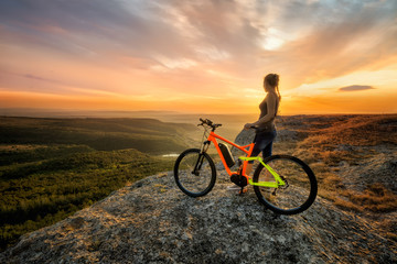 Fototapeta na wymiar Sunset from the top / A woman with a bike enjoys the view of sunset over an autumn forest