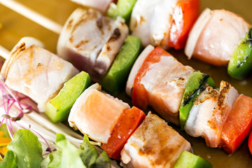 Close-up skewers fish steak on dish with vegetables