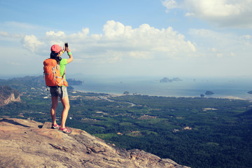 hiker taking photo with smartphone at seaside mountain cliff