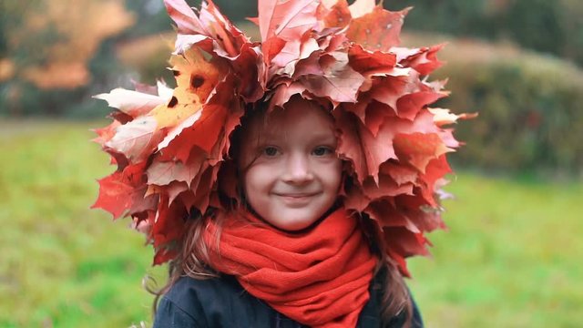 close-up portrait of happy smiling beautiful cute little girl in a wreath crown of autumn maple leaves slow motion