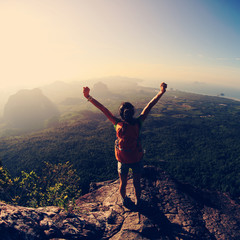 silhouette of free cheering woman hiker open arms at mountain peak